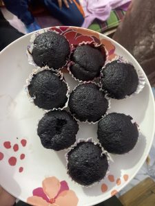 A plate with eight dark chocolate cupcakes in colorful paper liners, arranged neatly. The plate is white with red and orange floral designs.