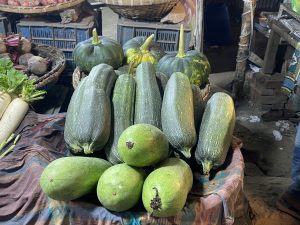 A market stall displays green zucchinis and squash arranged neatly on a cloth. The fresh vegetables are highlighted by soft lighting, creating a rustic, vibrant atmosphere.