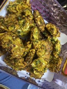 A tray filled with golden-brown vegetable pakoras, crispy and textured, with hints of green herbs, sits on white paper. 