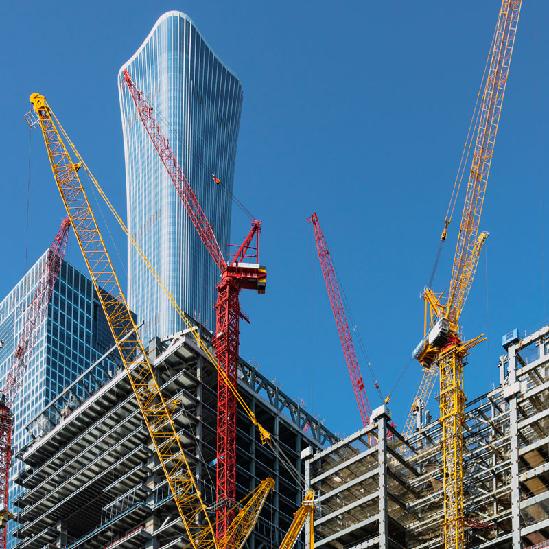 Construction-Box-Image Multiple yellow and red construction cranes operating around the steel skeleton of a new skyscraper.