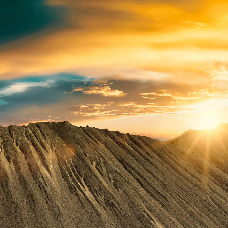 Mining-Box-Image A large mound of mined grey aggregate at a quarry site under a bright sunset.